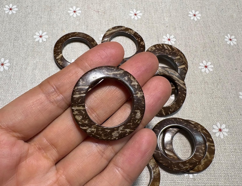 Puede incluir: Una colecci&oacute;n de anillos de madera circulares marrones con un patr&oacute;n natural y texturizado. Los anillos se sostienen en una mano, mostrando su tama&ntilde;o y dise&ntilde;o. Los anillos son probablemente para manualidades o decoraci&oacute;n del hogar.