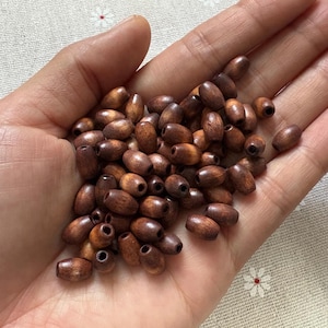Peut inclure: Gros plan sur une poignée de perles en bois ovales de différentes nuances de brun. Chaque perle est percée d'un trou central, idéal pour l'enfilage. Les perles sont lisses et semblent être en bois naturel, parfaites pour la création de bijoux ou l'artisanat.