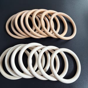Puede incluir: Dos conjuntos de anillos de madera, uno en marrón claro y otro en crema. Los anillos son lisos y circulares, perfectos para manualidades. La fila superior tiene un tono de madera natural, mientras que la fila inferior tiene un tono más claro, casi blanco.