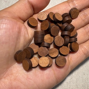 Peut inclure: Gros plan sur une main tenant plusieurs chevilles en bois rondes de différentes nuances de brun. Les chevilles, avec des motifs de grain de bois visibles, sont probablement destinées à des projets de meubles ou d'artisanat.