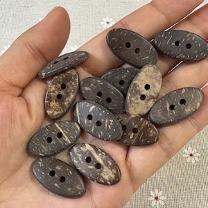 Può includere: Un gruppo di bottoni ovali a due fori, realizzati con gusci di cocco naturali. I bottoni presentano diverse tonalità di marrone e beige, con venature del legno e texture visibili. Ideali per cucito e progetti artigianali.