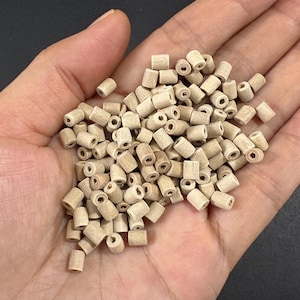 May include: A handful of small, cylindrical wooden beads. Each bead is light brown with a hole running through the center. The beads are uniform in size and shape, and appear to be unfinished.
