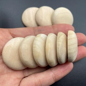 Może przedstawiać: Prezentacja kolekcji niedokończonych, naturalnych drewnianych krążków, częściowo całych, a częściowo przeciętych na pół. Krążki mają jasnobeżowy kolor i gładką, szlifowaną powierzchnię. Prawdopodobnie przeznaczone do projektów rzemieślniczych lub DIY.