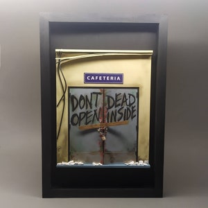 Puede incluir: Un diorama enmarcado de una puerta con un letrero que dice "No abrir, muertos adentro" y un letrero arriba que dice "Cafetería".