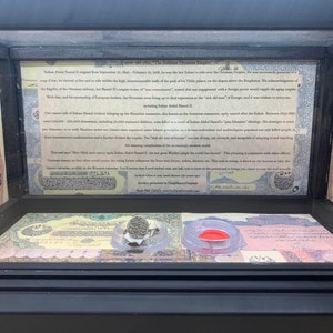 Op de afbeelding: Een ingelijste vitrine met een tekstpaneel over het Ottomaanse Rijk, met een citaat van Sultan Ahmed II. De vitrine bevat ook een kleine zilveren ring met een zegel en een rode waszegel.
