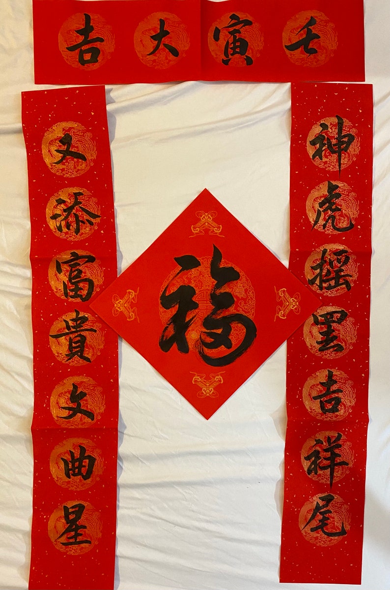 May include: Red and gold Chinese calligraphy scrolls with black ink. The scrolls feature traditional Chinese characters, including "福" (f&uacute;) meaning "good fortune" and "春" (chūn) meaning "spring".