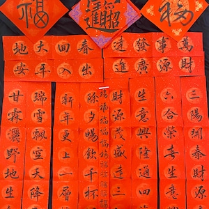 May include: Red and gold Chinese New Year calligraphy scrolls with black ink. The scrolls feature traditional Chinese characters and phrases, such as "prosperity", "wealth", and "good fortune".