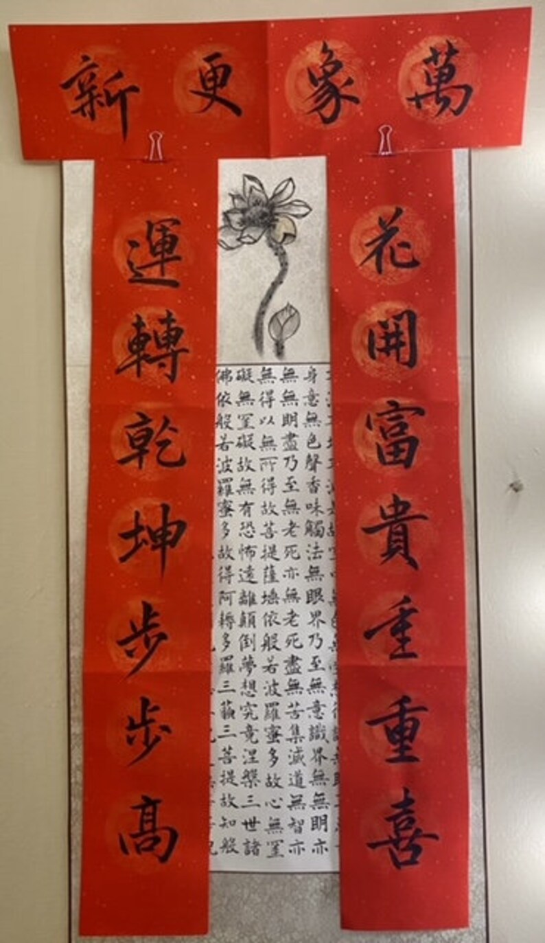May include: Red and white Chinese calligraphy scrolls with black ink. The scrolls feature the characters "新更家萬" and "花岡富貴重重喜" and a black ink drawing of a lotus flower.