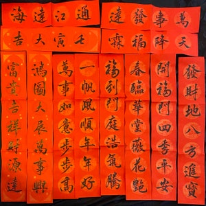 May include: A collection of 15 red paper scrolls with black Chinese calligraphy. The scrolls are arranged in three rows of five. The calligraphy includes phrases such as "good fortune", "prosperity", and "peace".