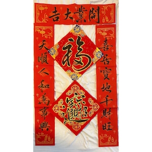 May include: Red and gold Chinese New Year decorations with calligraphy in black. The decorations feature the characters "福" (f&uacute;, meaning "fortune") and "春" (chūn, meaning "spring").