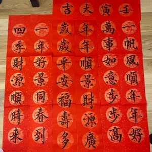 May include: Twenty red paper scrolls with black Chinese calligraphy. The scrolls are arranged in four rows of five. Each scroll has a different character written on it. The characters are: "吉", "大", "寅", "萬", "事", "如意", "步步", "高", "年", "年", "順", "景", "財源", "廣", "歲", "歲", "平安", "福壽", "多", "一年", "好景", "同", "春", "到", "四季", "財源", "順", "時", "來".