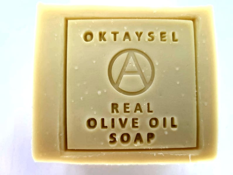 May include: A bar of Oktaysel Real Olive Oil Soap. The soap is white and has a rectangular shape. The brand name is printed on the front of the soap in a black font.