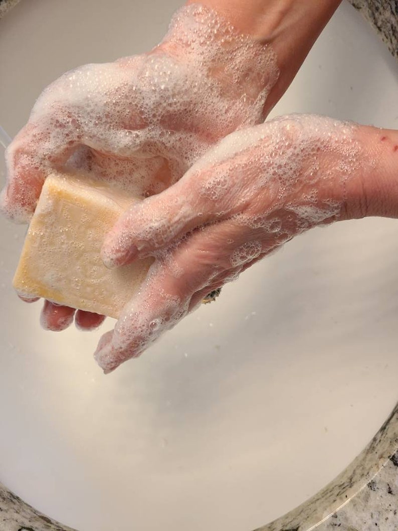May include: A person's hands are covered in white soap suds as they rub a rectangular bar of soap.