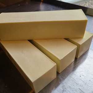 May include: Four bars of white soap stacked on top of each other on a silver surface.