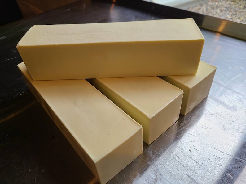 May include: Four bars of white soap stacked on top of each other on a silver surface.