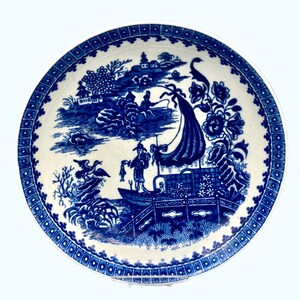 May include: Blue and white porcelain saucer with a traditional Chinese design featuring a boat, a bridge, and a figure fishing. The design is surrounded by a blue and white border.