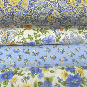May include: Three pieces of fabric with different floral patterns. The top fabric has a blue and yellow paisley pattern. The middle fabric has a white background with blue and yellow floral designs. The bottom fabric has a white background with blue and yellow floral designs.