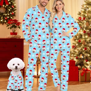 May include: Matching light blue pajama sets featuring a repeating pattern of white snowflakes and golden retriever dog faces wearing red Santa hats. The set includes long-sleeved button-down tops and long pants, plus a small dog shirt.