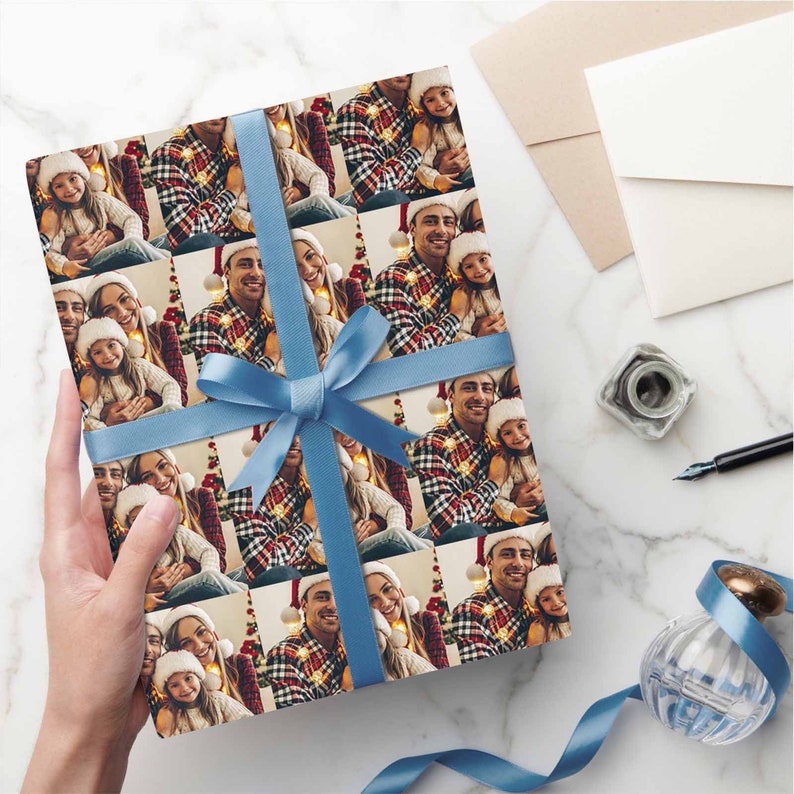 K&ouml;nnte beinhalten: Ein Blatt Geschenkpapier mit einem sich wiederholenden Muster einer dreik&ouml;pfigen Familie, die f&uuml;r ein Weihnachtsfoto posiert. Die Familie tr&auml;gt festliche Kleidung und l&auml;chelt. Das Geschenkpapier ist mit einem blauen Band gebunden.