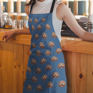May include: A blue denim apron with a repeating pattern of a dog's face. The dog has brown fur and is looking directly at the camera.