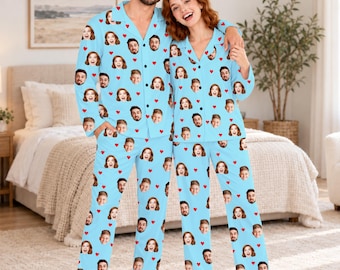 May include: Matching light blue pajama sets featuring a repeating pattern of two different faces and small red hearts. Each set consists of a long-sleeved button-down shirt with a collar and matching long pants with an elasticized waistband.
