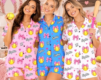May include: Three matching pajama sets in pink, blue, and white, each featuring a repeating pattern of yellow softballs with pink polka-dot bows, the name Sophia, and the number 12. The shirts have collars and buttons down the front.