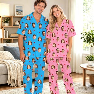 Könnte beinhalten: Ein passendes Pyjama-Set bestehend aus einem blauen Hemd mit Knopfleiste und Hose für eine Person sowie einem rosa Hemd mit Knopfleiste und Hose für eine andere. Beide Sets sind mit einem Muster aus kleinen roten Herzen und einem Gesicht bedruckt.