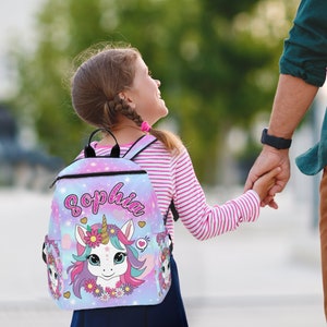 May include: A pink and blue backpack with a unicorn design and the name "Sophia" printed on it. The backpack has a zipper closure and adjustable straps.
