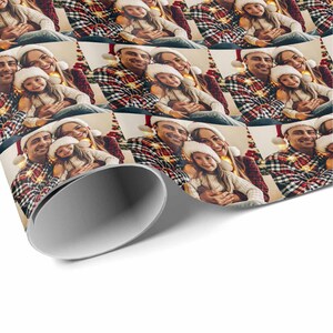 K&ouml;nnte beinhalten: Ein Weihnachtsgeschenkpapier mit einem Design, das eine dreik&ouml;pfige Familie zeigt, die Weihnachtsm&uuml;tzen tr&auml;gt und l&auml;chelt. Der Hintergrund ist ein rot-gr&uuml;nes Karomuster mit Weihnachtslichtern.