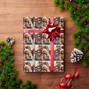 K&ouml;nnte beinhalten: Weihnachtsgeschenkpapier mit einem sich wiederholenden Muster einer dreik&ouml;pfigen Familie, einem Mann, einer Frau und einem M&auml;dchen, die Weihnachtsm&uuml;tzen tragen und l&auml;cheln. Das Papier ist mit rotem Band und einer roten Schleife verziert.