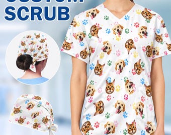 May include: A white V-neck scrub top and matching scrub cap featuring a repeating pattern of dog and cat faces interspersed with colorful paw prints. The set includes a short-sleeved top and a tie-back cap with a gathered design.