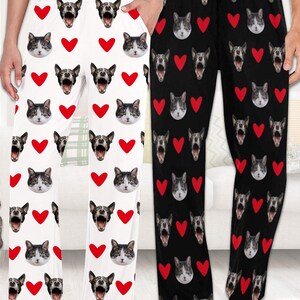 May include: Two pairs of pajama pants with a repeating pattern of red hearts and animal faces. One pair is white with black and white cat faces, the other is black with black and white dog faces.