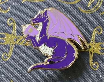 Pin de esmalte duro con forma de dragón leyendo un libro