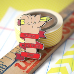 May include: Red enamel pin with a cartoon fist holding a yellow pencil. The pin has three red banners with the text "Teachers We Get The Job Done".