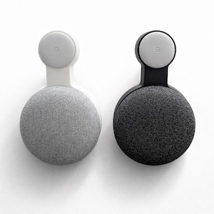 May include: Two smart home speakers, one grey and one black, mounted on a wall. The speakers have a circular design with a fabric cover and a small, round top with the Google logo.