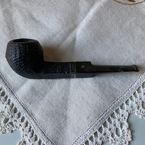 May include: A black briar pipe with a rough, textured finish. The pipe has a silver band with the inscription "90".