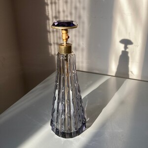 May include: A vintage glass perfume bottle with a textured, ribbed design. The bottle has a clear glass body and a purple glass stopper.