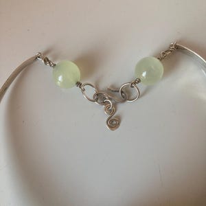 May include: A silver bracelet with a clasp and two light green beads. The bracelet is made of wire and has a simple design.