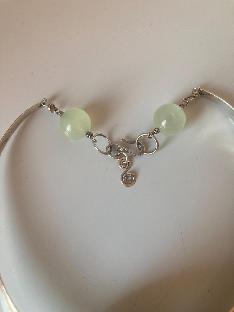 May include: A silver bracelet with a clasp and two light green beads. The bracelet is made of wire and has a simple design.