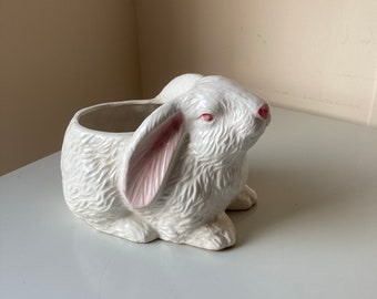 May include: White ceramic planter shaped like a rabbit with pink ears. The planter has a textured surface that resembles fur.