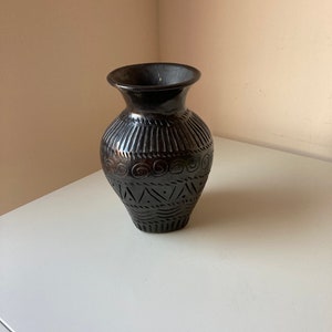 以下が含まれることがあります： 複雑な彫刻が施された黒い陶器の花瓶。花瓶は丸みを帯びたボディと狭い開口部を持っています。