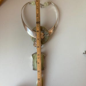 May include: A silver and green jade necklace with a large pendant. The pendant is a circle with a smaller circle inside. The necklace is 13 inches long.
