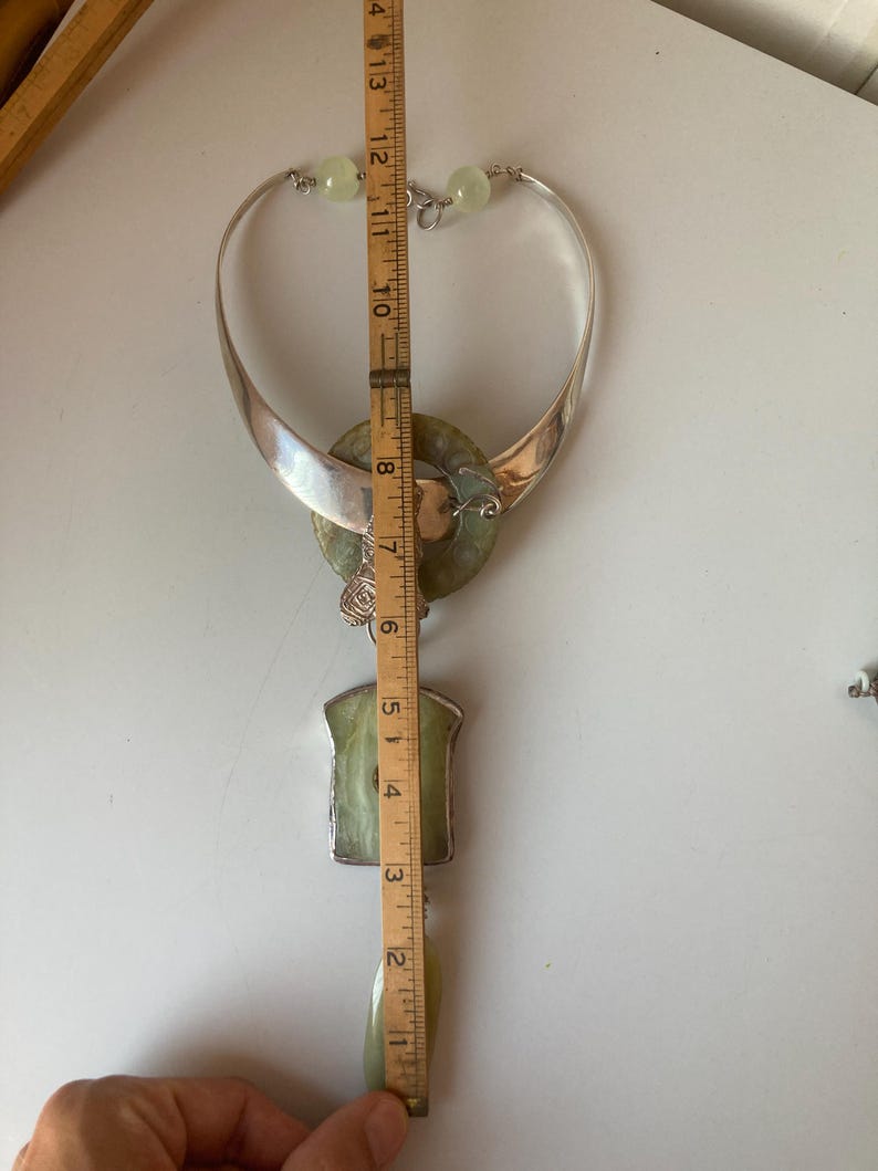 May include: A silver and green jade necklace with a large pendant. The pendant is a circle with a smaller circle inside. The necklace is 13 inches long.