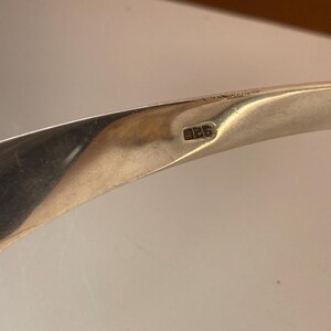May include: Close-up of a silver bracelet with the number "925" stamped on the inside. The bracelet is curved and has a smooth, polished finish.