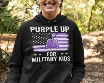 Op de afbeelding: Zwart hoodie met een Purple Up for Military Kids ontwerp. Het ontwerp bevat een paarse Amerikaanse vlag met twee paarse hondenlabels die eraan hangen.