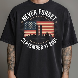 Puede incluir: Camiseta negra con un gráfico que conmemora el 11 de septiembre de 2001. El diseño presenta la bandera estadounidense, las Torres Gemelas y las palabras "Never Forget" y "September 11, 2001" en un círculo.