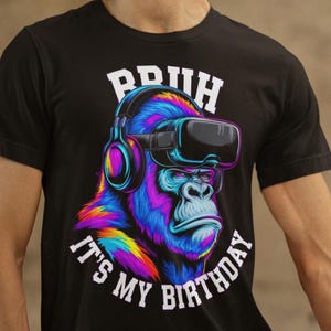 Può includere: T-shirt nero con un gorilla colorato che indossa un visore VR e cuffie. Il testo "BRUH" è sopra il gorilla e "IT'S MY BIRTHDAY" sotto. Il gorilla ha la pelliccia blu, viola e gialla.
