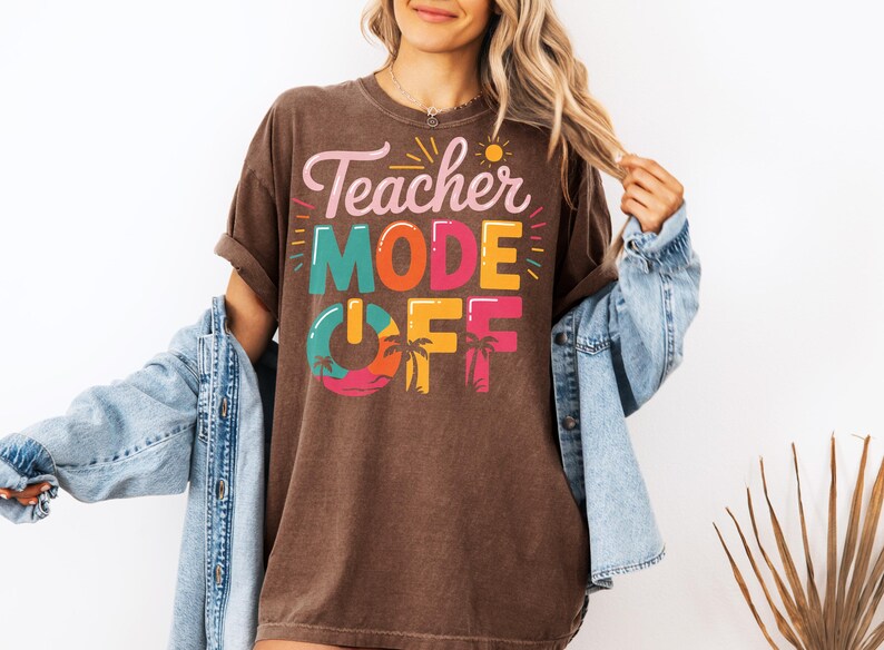 Peut inclure: Un t-shirt marron avec le texte "Teacher Mode Off" en lettres color&eacute;es. Le texte est entour&eacute; de palmiers et d'un soleil.