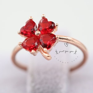 Puede incluir: Un anillo de oro con un diseño de trébol de cuatro hojas con piedras rojas en forma de corazón. El anillo tiene la inscripción "just for you" grabada en la banda.