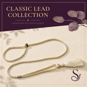 Può includere: Un guinzaglio da esposizione intrecciato color beige con una nappa decorativa a un'estremità, una piccola perlina scorrevole nera e un inserto metallico. Il testo CLASSIC LEAD COLLECTION e HANDCRAFTED SHOW LEADS è visibile in alto.